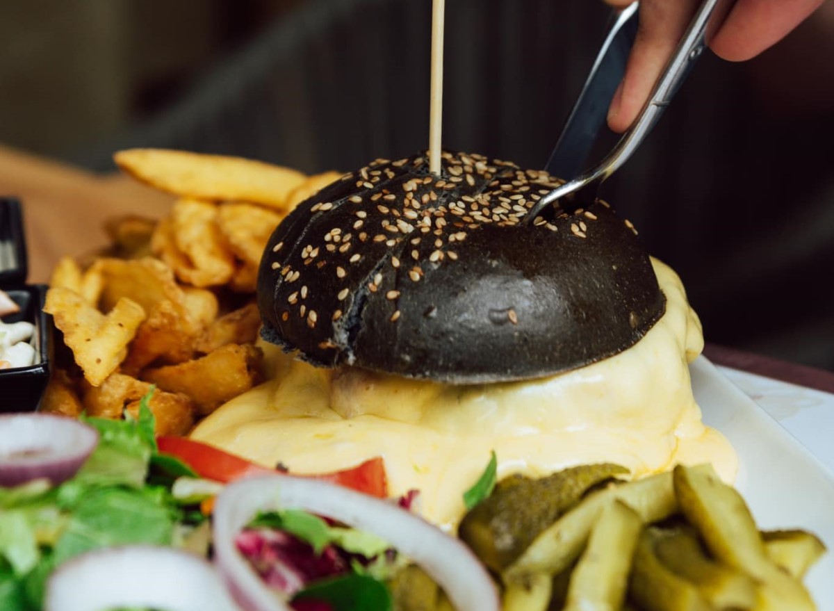 burger cu chifla neagra si melted cheese, alaturi de cartofi, ceapa si castraveti murati, asezate separat