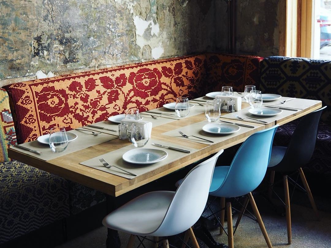 masa de lemn cu scaune moderne si bancuta acoperita cu stergar traditional, la Restaurant Mahala, unul din Restaurante din Bucureşti de recomandat unui turist