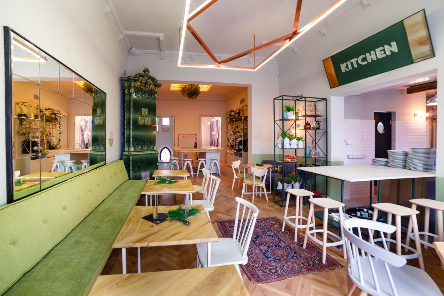 #AcasăLaSimbio imagine de ansamblu din restaurant Simbio, cu mai multe mese de lemn, o canapea lunga verde, pereti alba si o soba