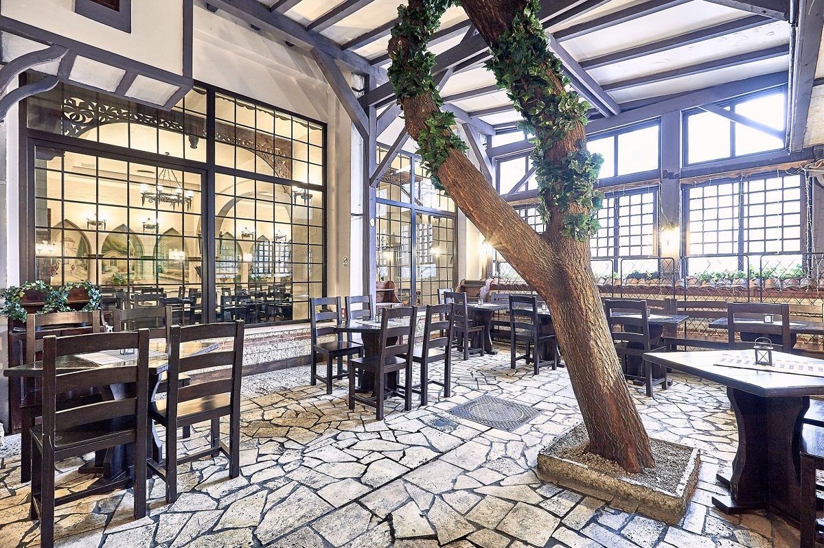 restaurantul Bistro Dorobanti, cu mese de 4 persoane, si scaune din lemn, cu geamuri mari, si un trunchi de copac care strapunge tavanul