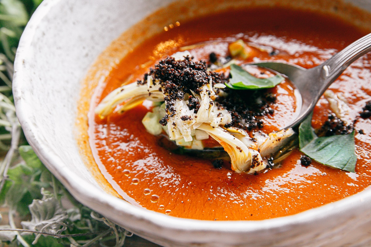 close up pe o farfurie alba plina cu gazpacho, supa crema de rosii, cu frunze de busuioc