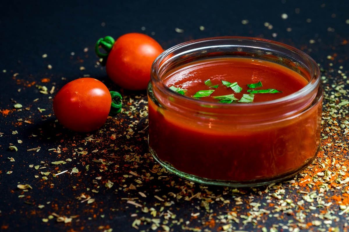 borcan scund cu salsa, fotografiat pe fundal negru, cu doua rosii cherry si semninte de ardei iute pe langa, unul din sosuri iuți faimoase