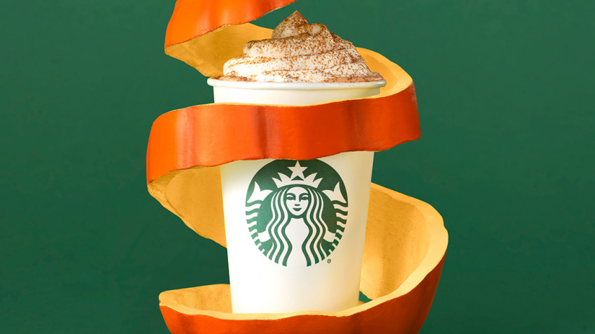 pahar cu pumpkin spice latte de la Starbucks, fotohgrafiat pe fundal verde inchis, si inconjurat de o spirala de coaja de dovleac