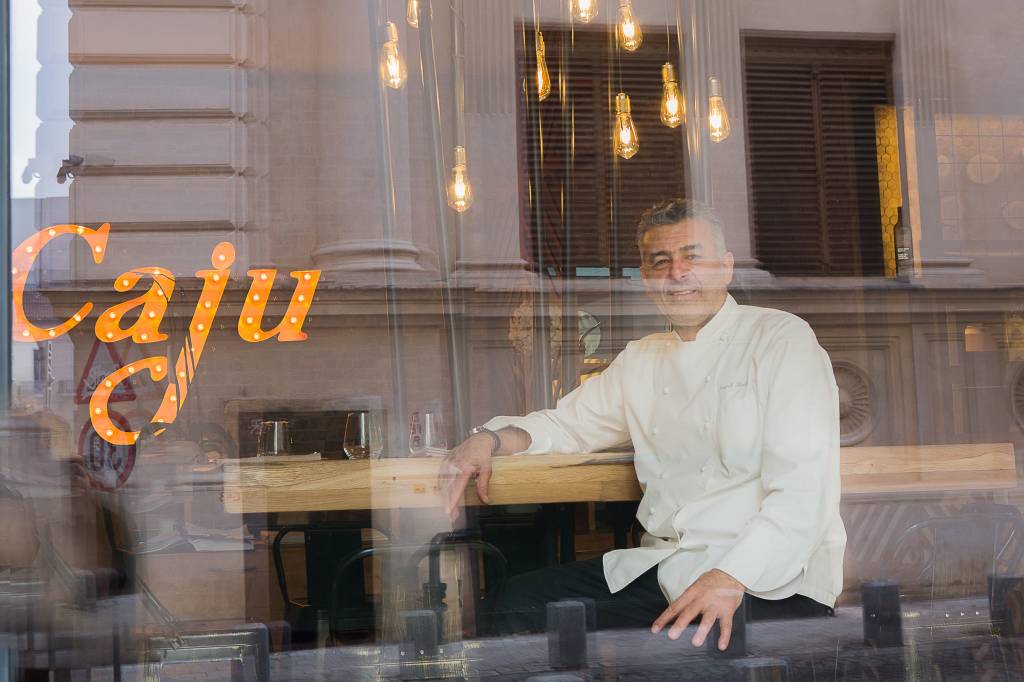 Chef Hadad fotografiat din afara in braseria Caju by Joseph Hadad \, in dreptul vitrinei, iar in fundal sigla braseriei luminatain dreptul vitrinei