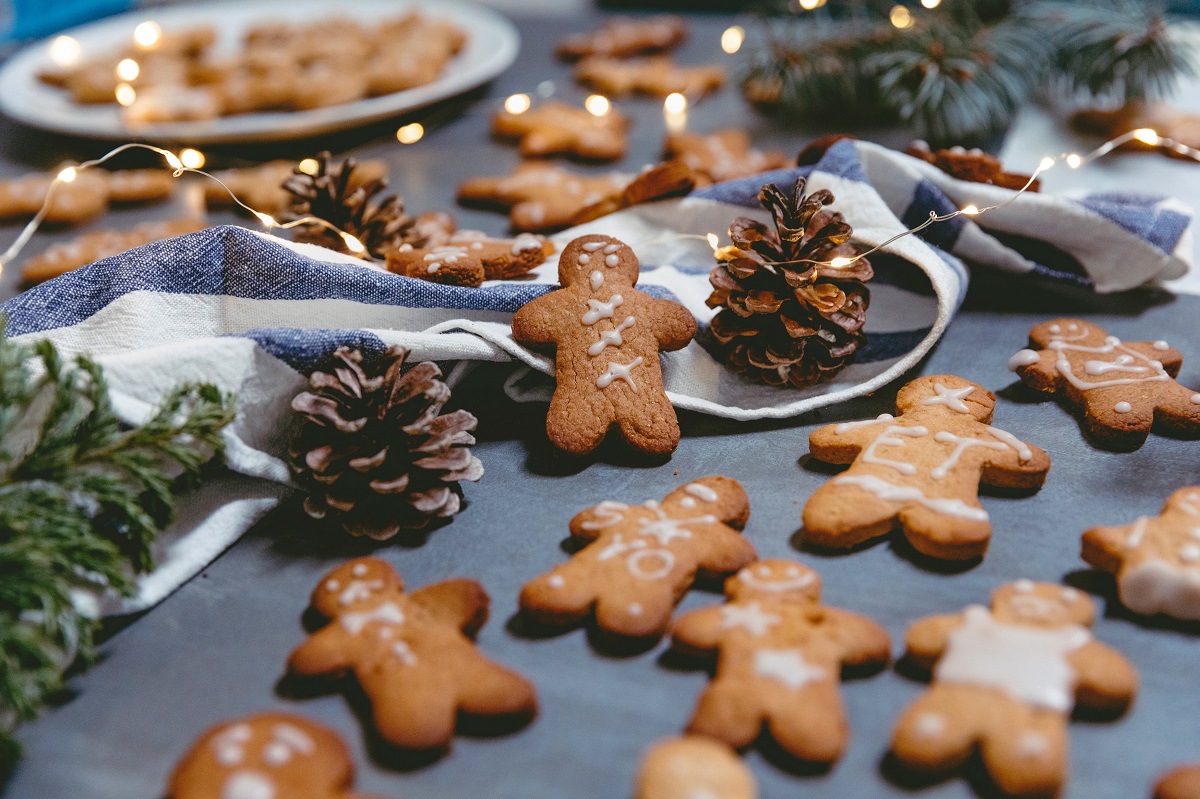 omuleí de turt[ dulce, imprastiati pe masa cu fundal gri, printre conuri de brad, panglica argintie si beculete, ca rețetă de biscuiți pentru Moș Crăciun