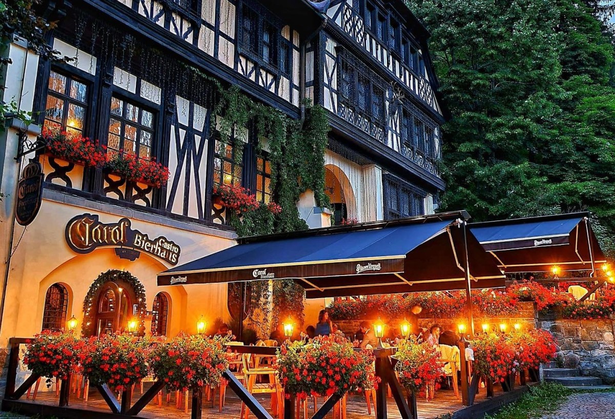 Restaurantul Carol Gastro Bierhaus fotografiat de afara, cu design baverz, varuit alb cu barne de lemn decorative si terasa cu ghivece de muscate rosii, unul din cele mai bune restaurante din Sinaia