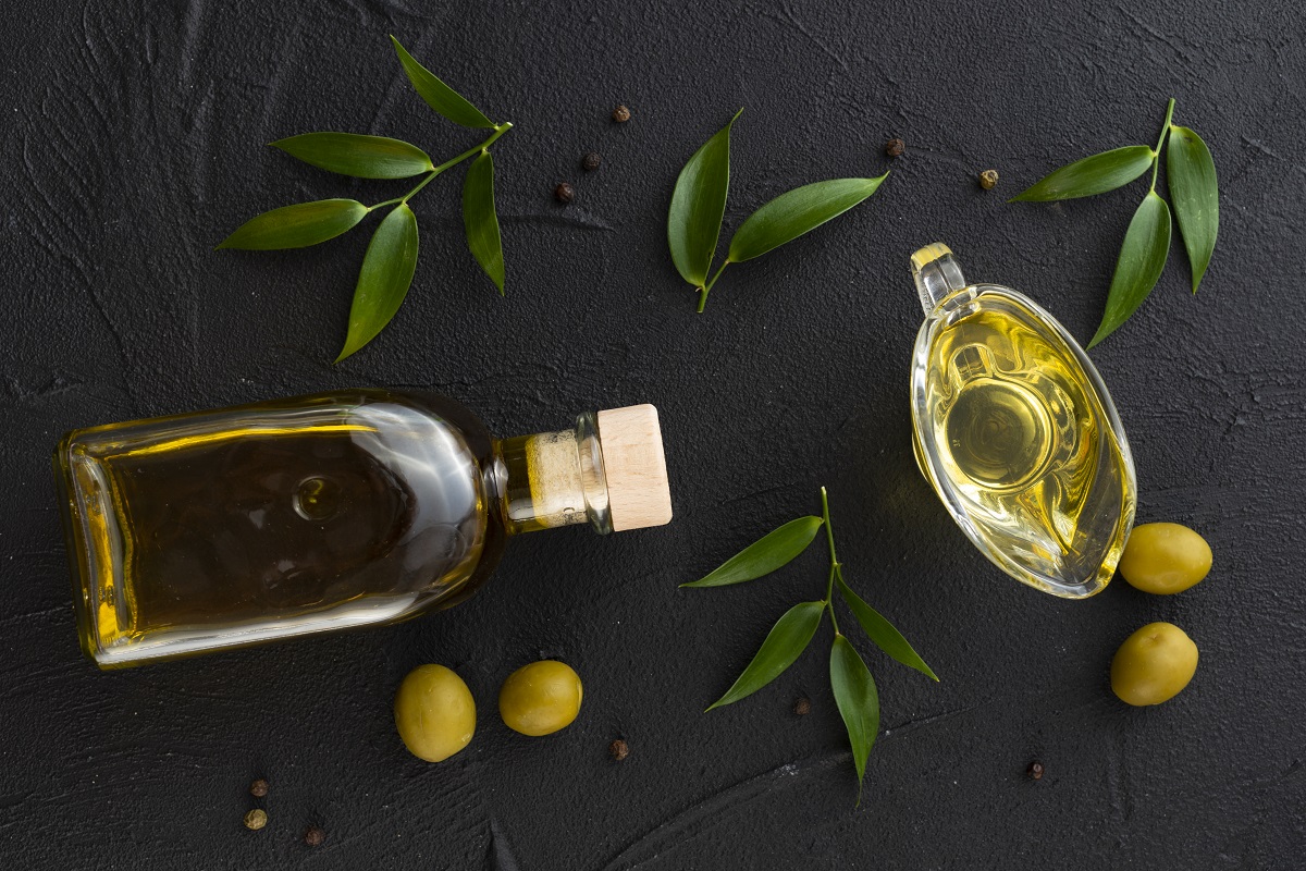 sticla de ilei de masline, alaturi de masline verzi, frunze de maslin si un bol cu ulei, toate pe fundal negreu, fotografiate de sus, imagine reprezentativa pentru cum alegi cel mai bun ulei de măsline