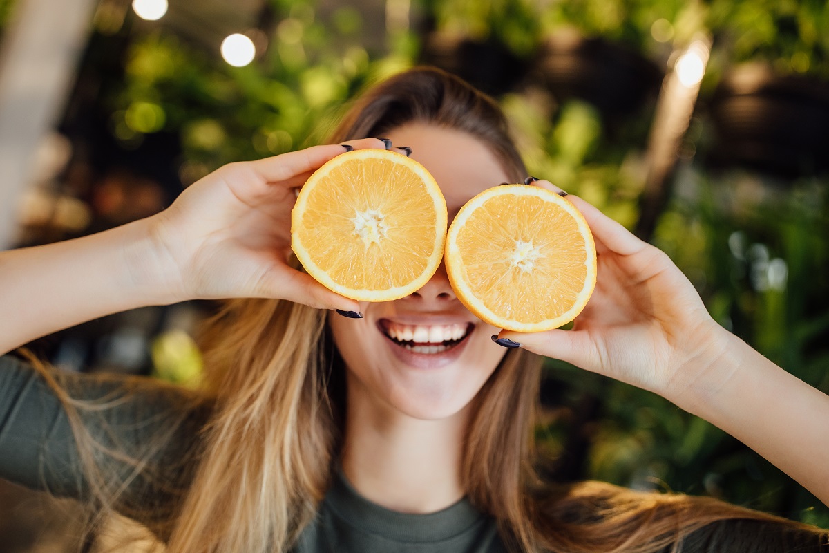 Alimentație echilibrată după sărbători: Happy young caucasian woman holding fresh oranges in front of eyes and smiling.