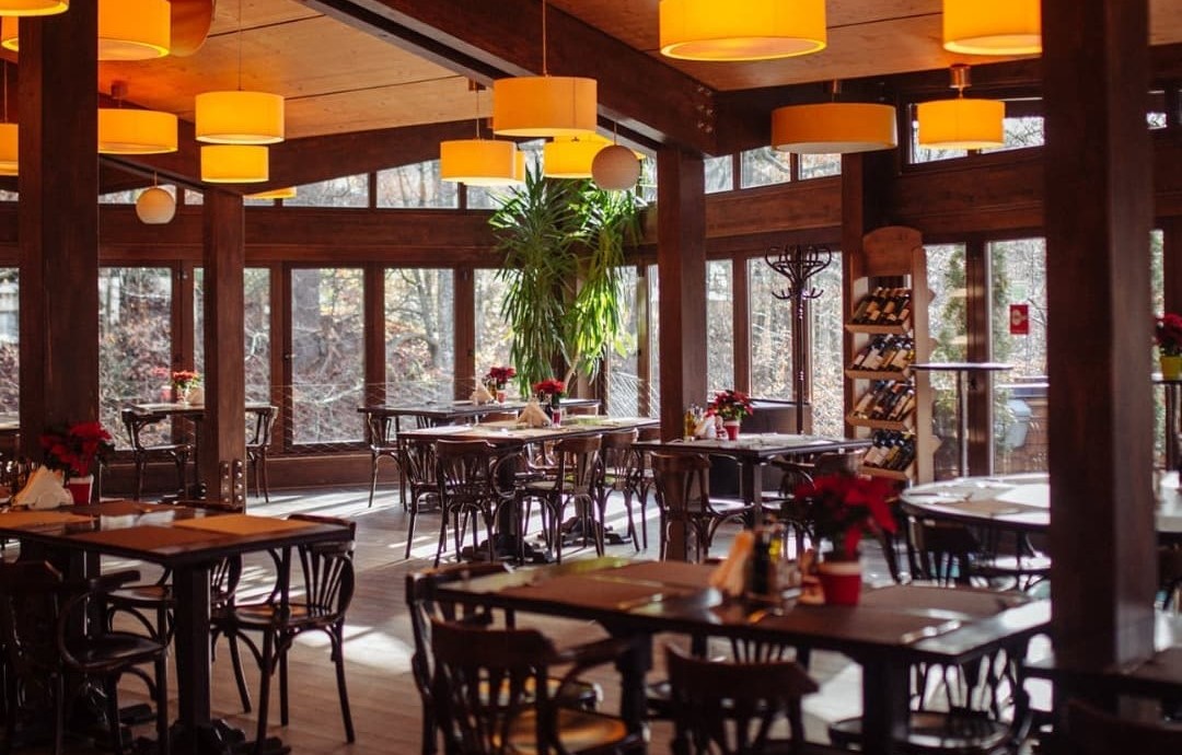 Kuib Restaurant din sinaia, cu mese din lemn si corpuri de iluminat suspendate, galbene, si ferestre mari prin care se vede padurea
