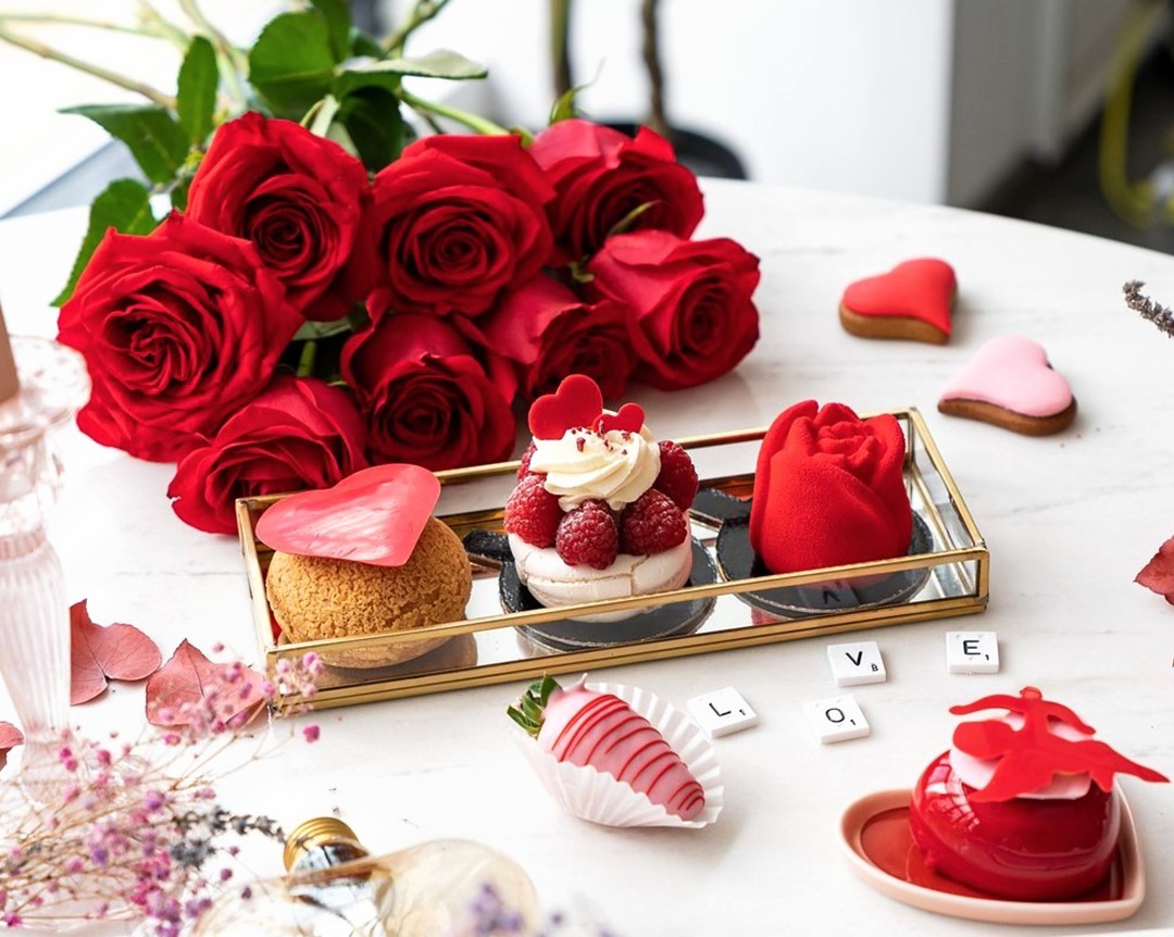 trei prajituri de la Grace Couture Cakes, asezate pe o tava, in spate cu un buchet de trandafiri roșii, un loc de unde să îi faci cadou de Ziua Îndrăgostiților ceva dulce