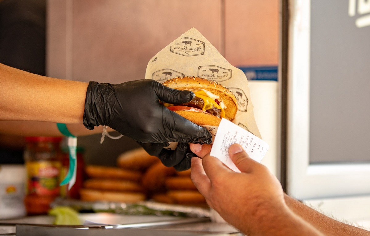 close up pe maini cu un vanzator care ofera un burger impachetat unui cumparator, la Bucharest Street Food Festival