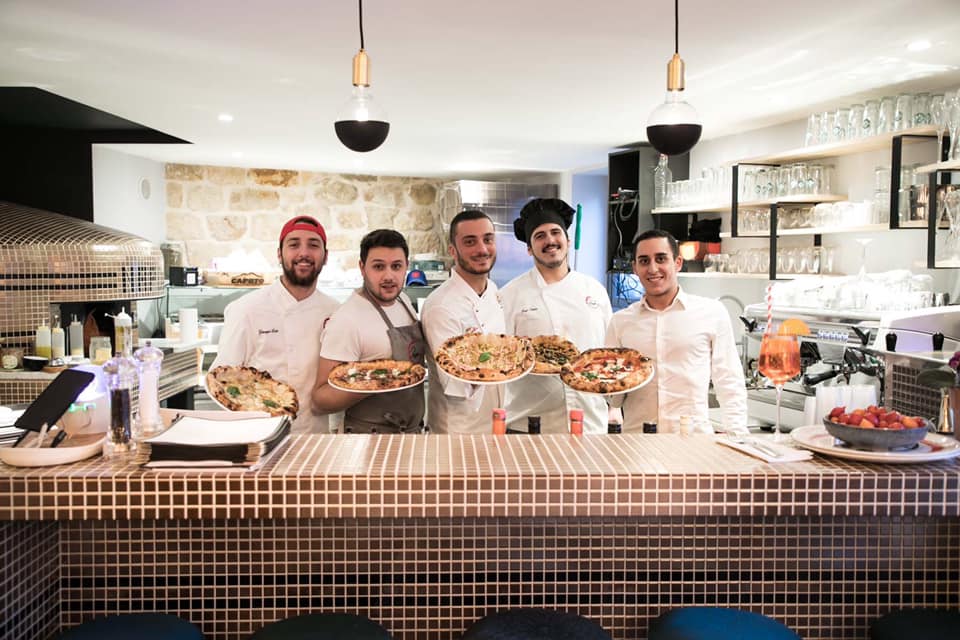 echipa de bucatari le Pepper Paris, una din cele mai bune pizzerii din Europa, cu cate o pizza in mana, stand in spatele tejghelei