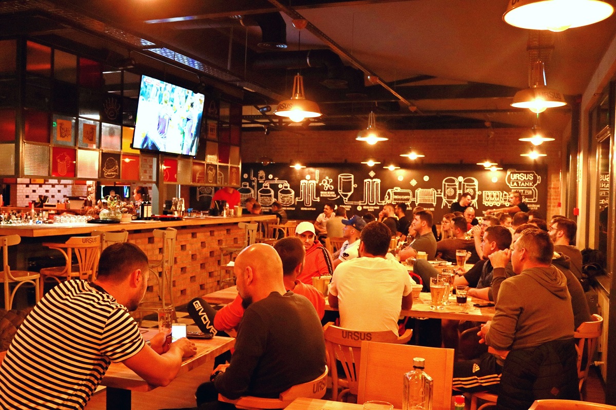 multi barbati asezati la mese in restaurant Draft Pub Tankeria Ursus din București, urmarind un meci difuzat la TV