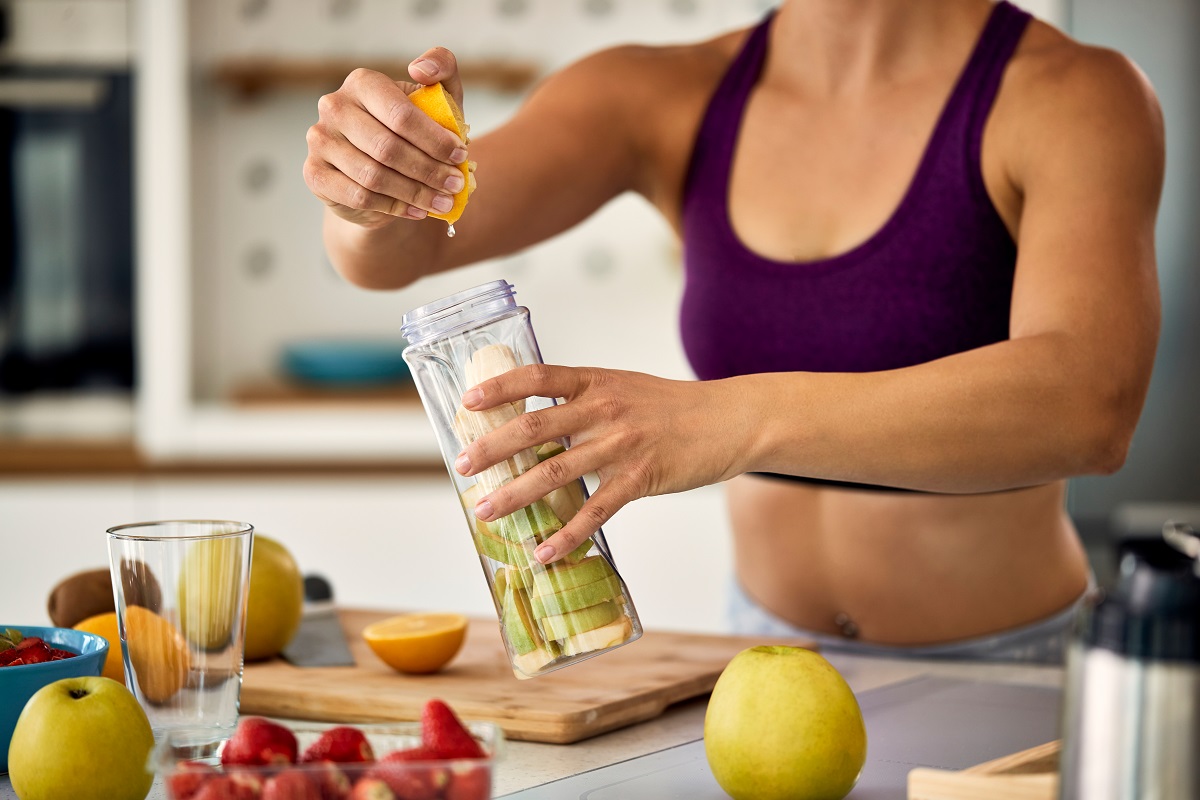 Unrecognizable sportswoman using lemon while making fruit smoothie at home.