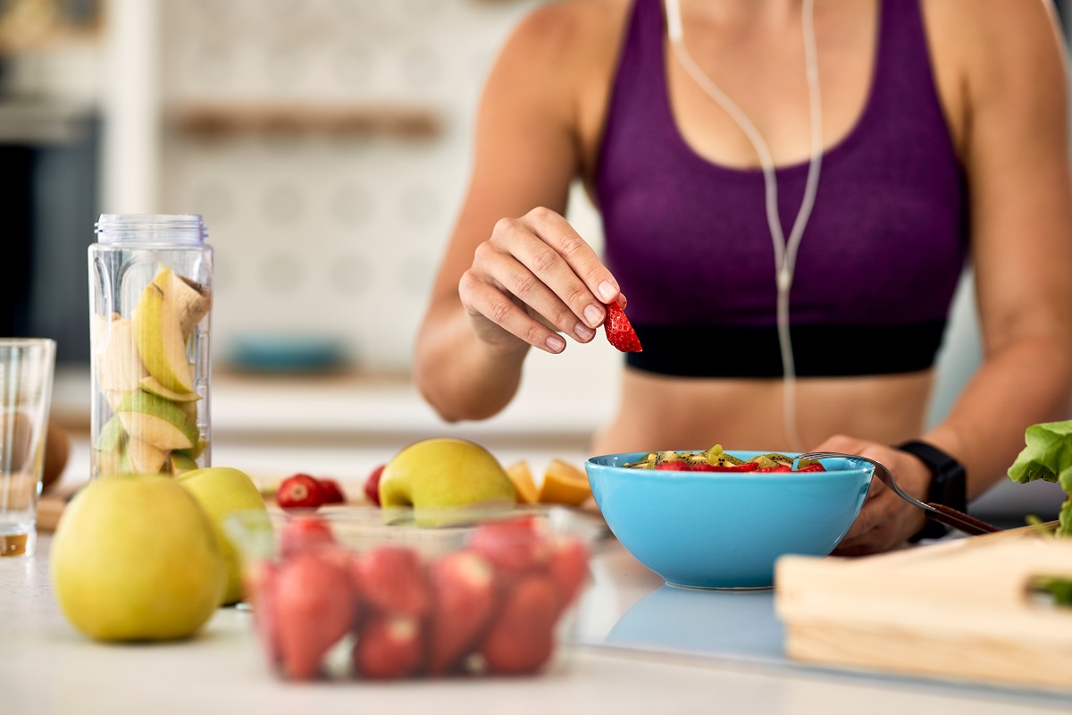Close-up of athletic woman adding strawberries while making fruit salad in the kitchen. Imagine sugestivă pentru ce alimente să mănănci după alergare
