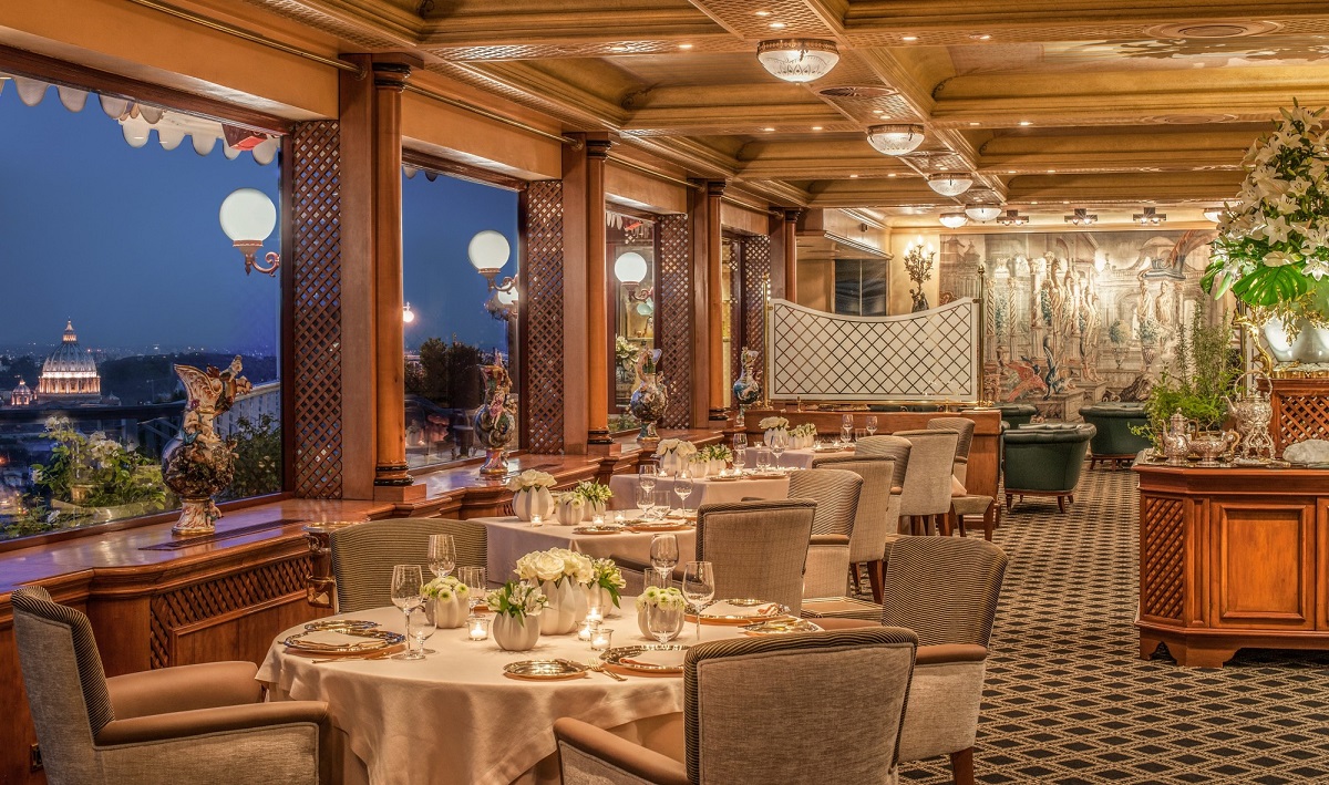 imagine de ansamblu din restaurant La Pergola, cu mese rotunde elegante, asezata in fata geamurilor mare cu lumini aprinse, seara, si cu tapiterii in fundal, un restaurant de 3 stele Michelin de la Londra