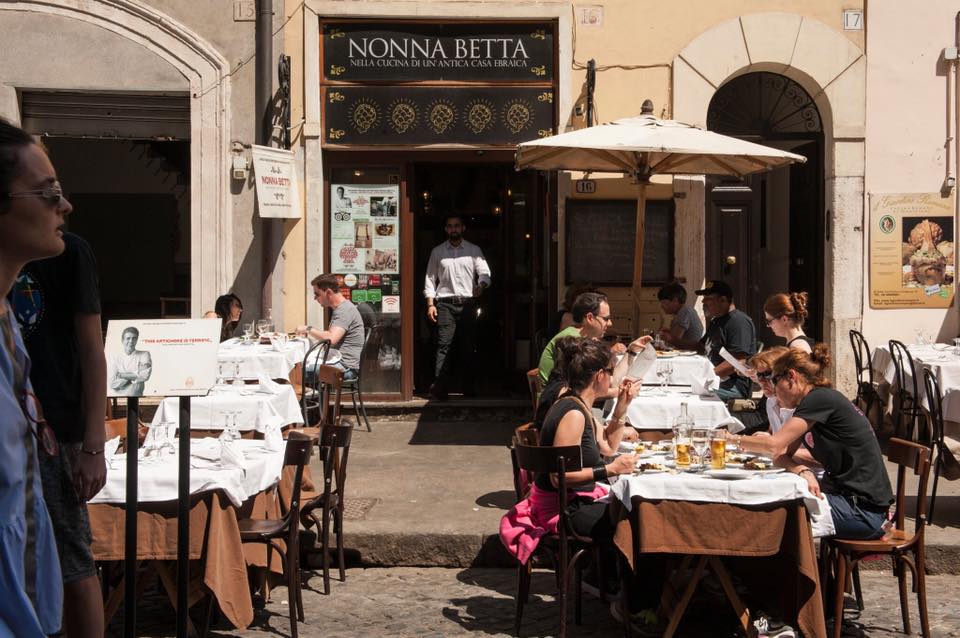 terasa restaurantului Nonna Betta din Roma, cu oameni asezati la mese afara, pe strada, iar in fundal intrarea in restaurant, unul dintre cele mai bune restaurante de la Roma