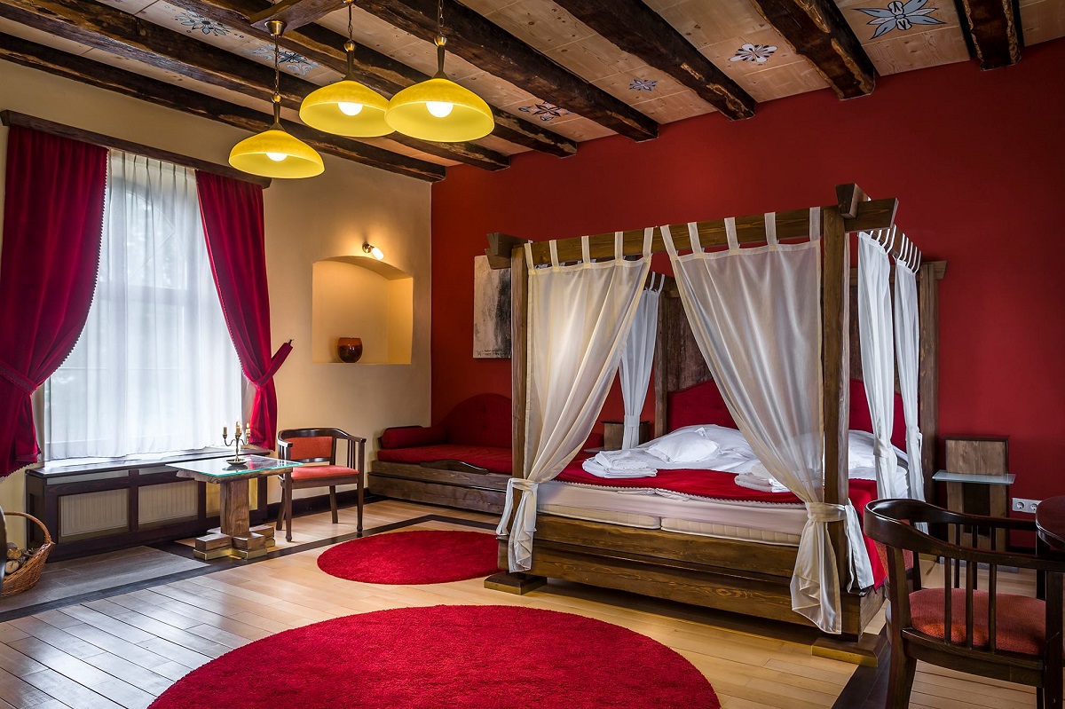 dormitor cu baldachin, pereti rosii , barne de lemn si draperii din catifea rosie la Castel Daniel, unul din conace din România