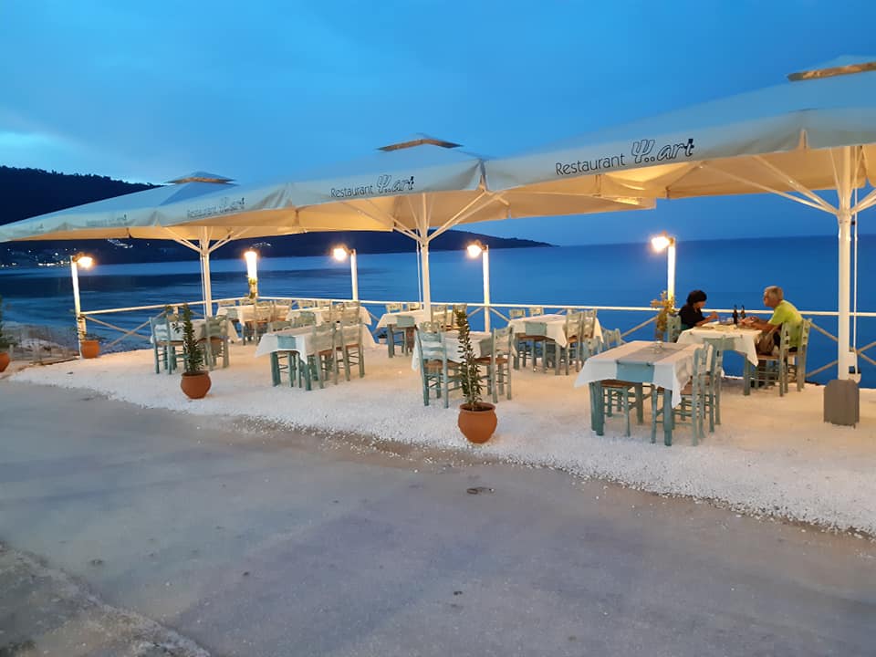 Taverna Fish Art din Skala Potamia, cu mese mici si umbrele mari, fotografiata seara, cu lumini aprinse
