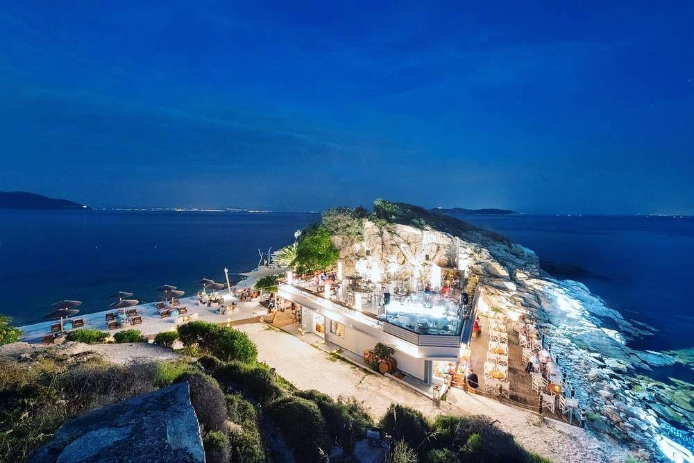 imagine de ansamblu cu localul Karnagio, din lista de taverne și restaurante bune în Thassos, fotografiat seara, iluminat puternic, cu marea de o parte si alta a coastei