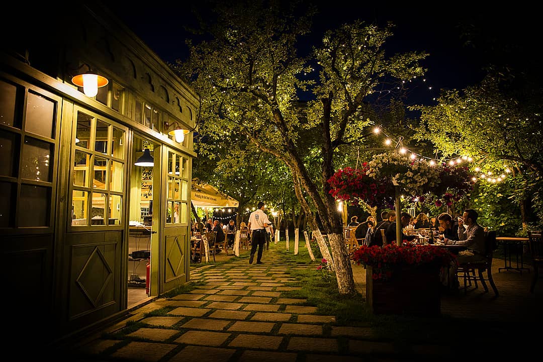 Terasa de la restaurant Livada din Cluj, fotografiata noaptea, cu luiminite decorative, copaci si flori si oameni asezati la mese