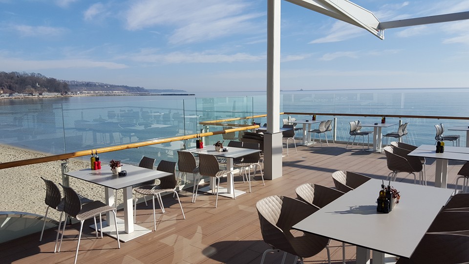 terasa cu mese albe si scaune moderne si parapet din sticla dincolo de care se vedee marea la The Sea Terrace, unul dintre cele mai bune restaurante pe de plitoralul bulgăresc