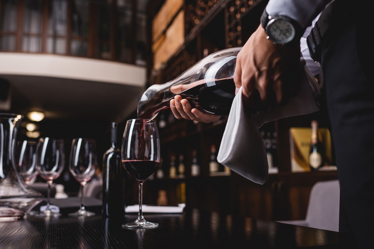 Selective focus of sommelier holding towel and pouring wine in glass on table in restaurant 