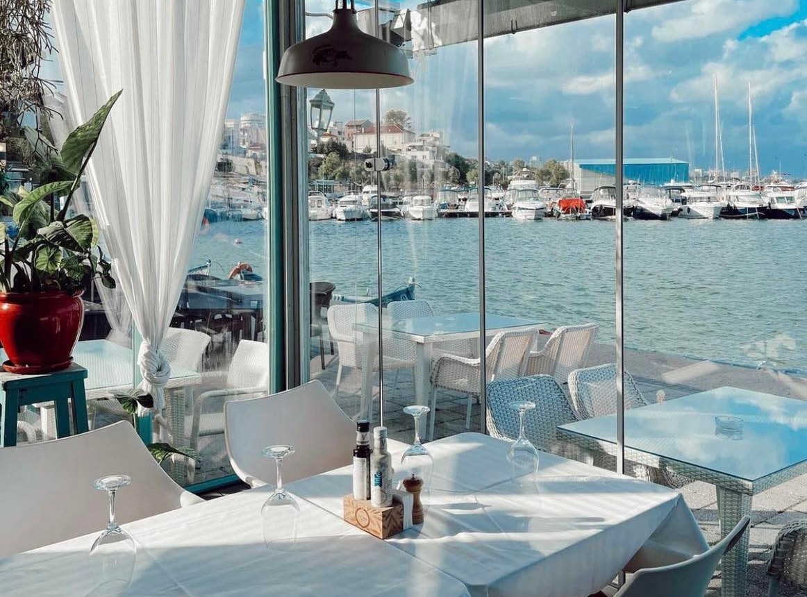 prim plan cu o masa la Bacaro, asezata in dreotul unor geamuri mari prin care se vede marea si mici ambarcatiuni, unul dintre cele mai bune restaurante din Constanța