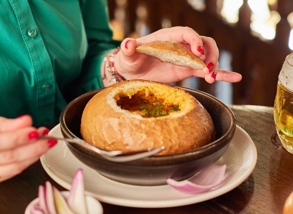 closeup cu o farfurie cu ciorba in paine din care serveste cu lingura o femeie, la Caru cu Bere