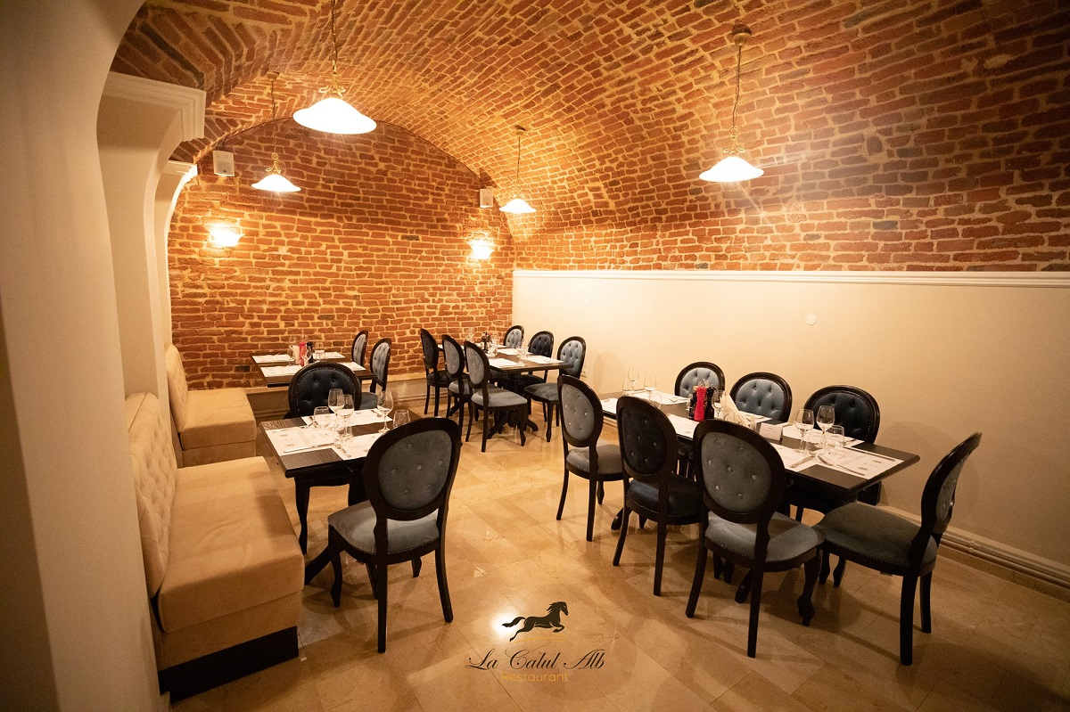 Incapere in Restaurant la Calul Alb, cu tavan boltit cu caramida aparenta si mese asezate pe langa pereti