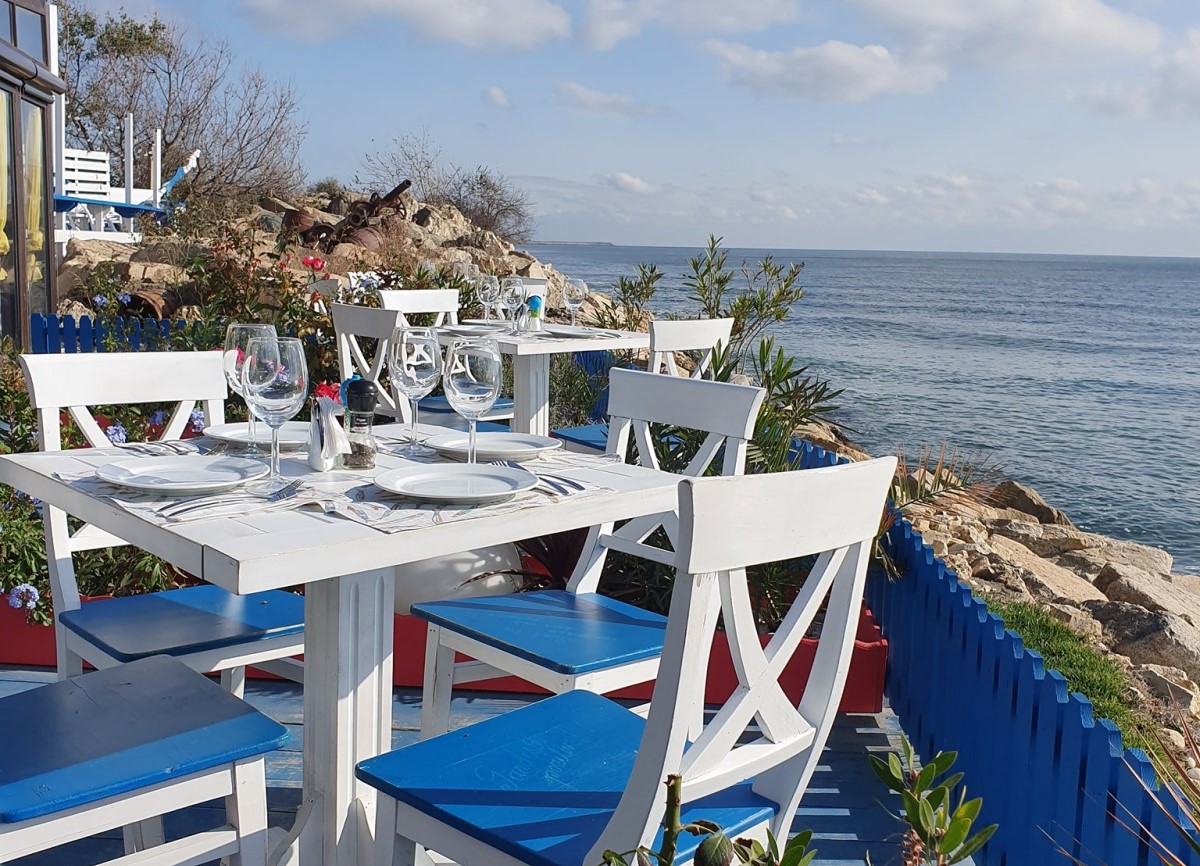 terasa pe malul marii, cu scaune albe cu albastru, la Pescaria lui Matei de la Agigea, unul dintre cele mai bune restaurante din Constanța