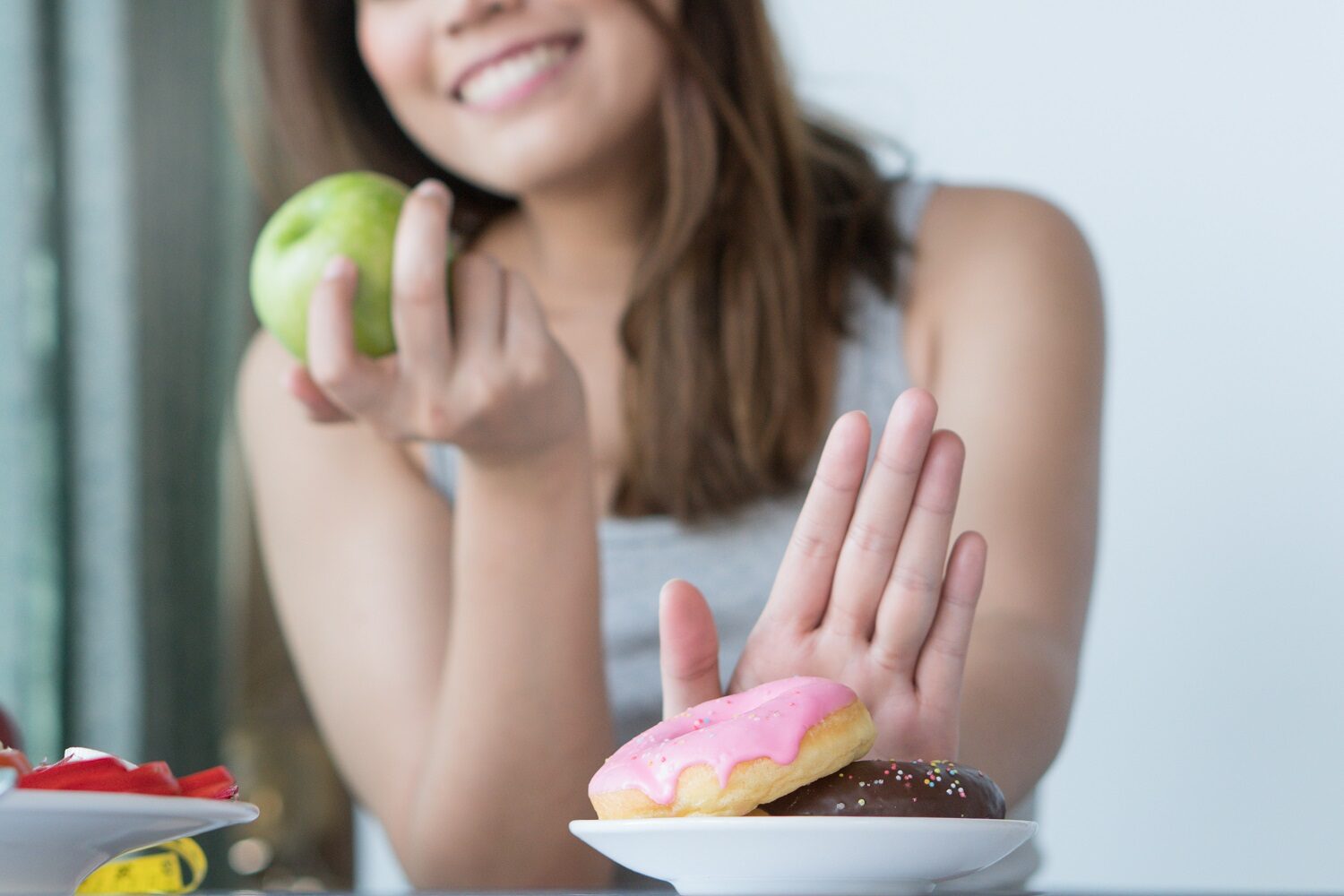 Woman on dieting for good health concept. Close up female using hand push out her favourite donut and choose green apple and vegetables for good health. Imagine reprezentativa pentru ce se întâmplă când nu mai mănânci zahăr