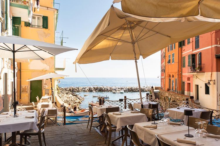 Dau Cila, unul din restaurante din Cinque Terre, cu mes si umbrele asezate pa malul marii, intre case colorate