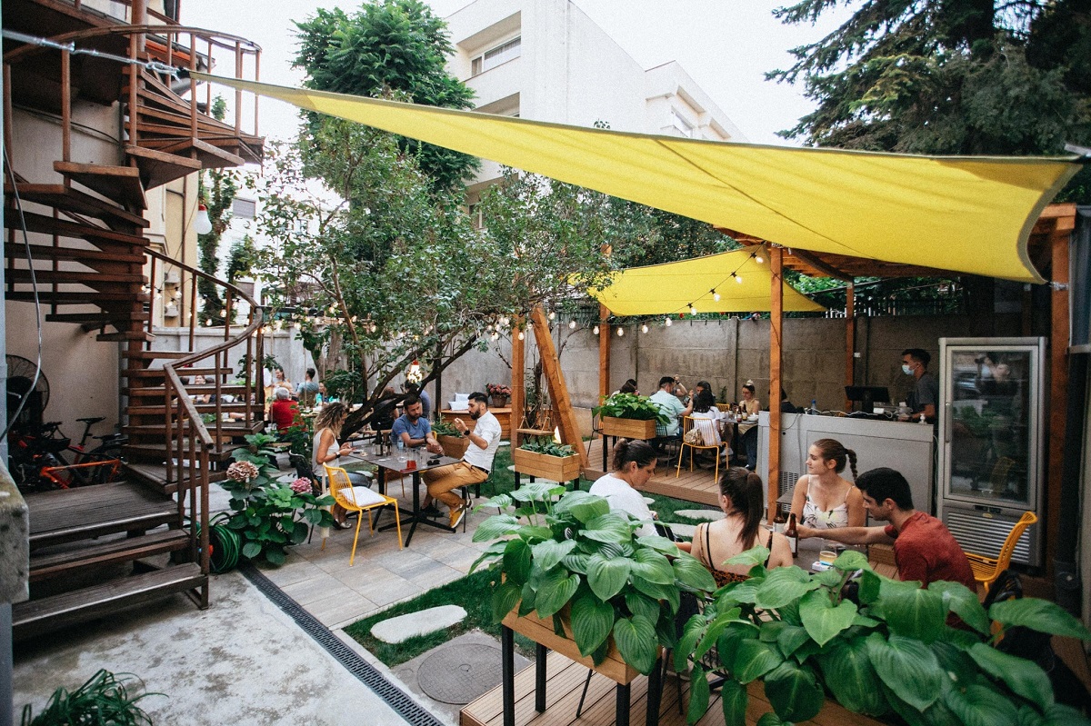 oameni la terasa la verv.kitchen unul din restaurante vegetariene din București, amenajată cu copertine galbene
