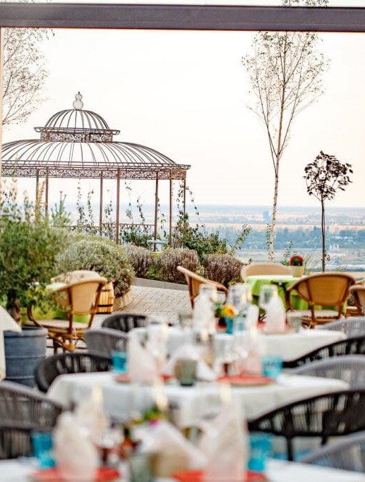 mese de restaurant in prim plan, si un foisor metalic cu priveliște panoramica asupra domeniului Casa Timis, una din destinații de tip retreat din România
