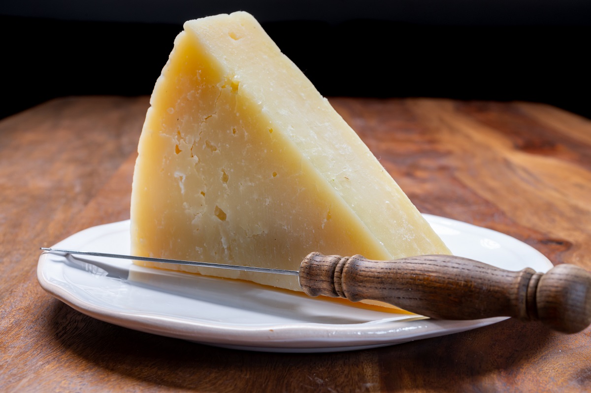 bucata triunghiulara de brânzaă Pecorino Romano, maturat, brânză tare din lapte de oaie, servita pe o farfurie alba, alturi de un cuțit pentru brânzeturi 