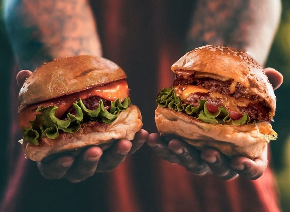 closeup cu un barbat cu tatuaje care intinde doi burgeri pe care ii tine in mana, de la Burger Van, unde mănânci cei mai buni burgeri din București