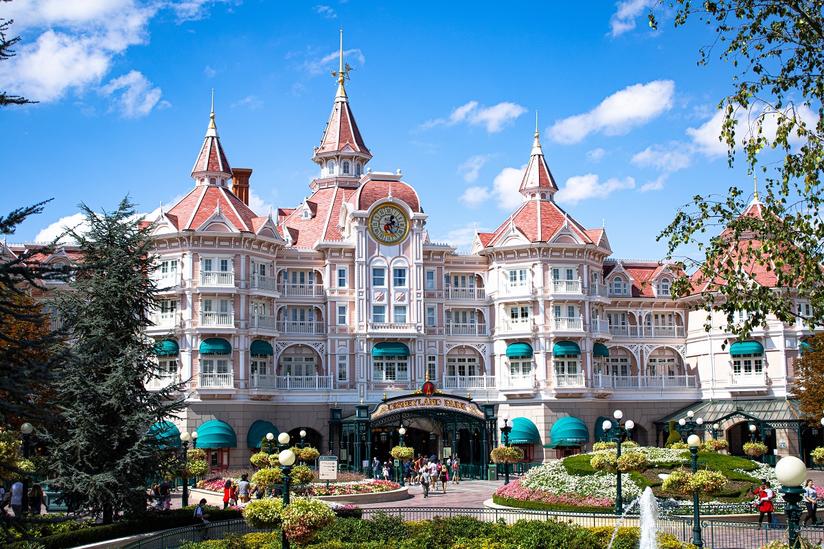 Privire de ansamblu asupra intrarii Disneyland park, o cșladire ca un castel, cu alei pline de verdeata in fata