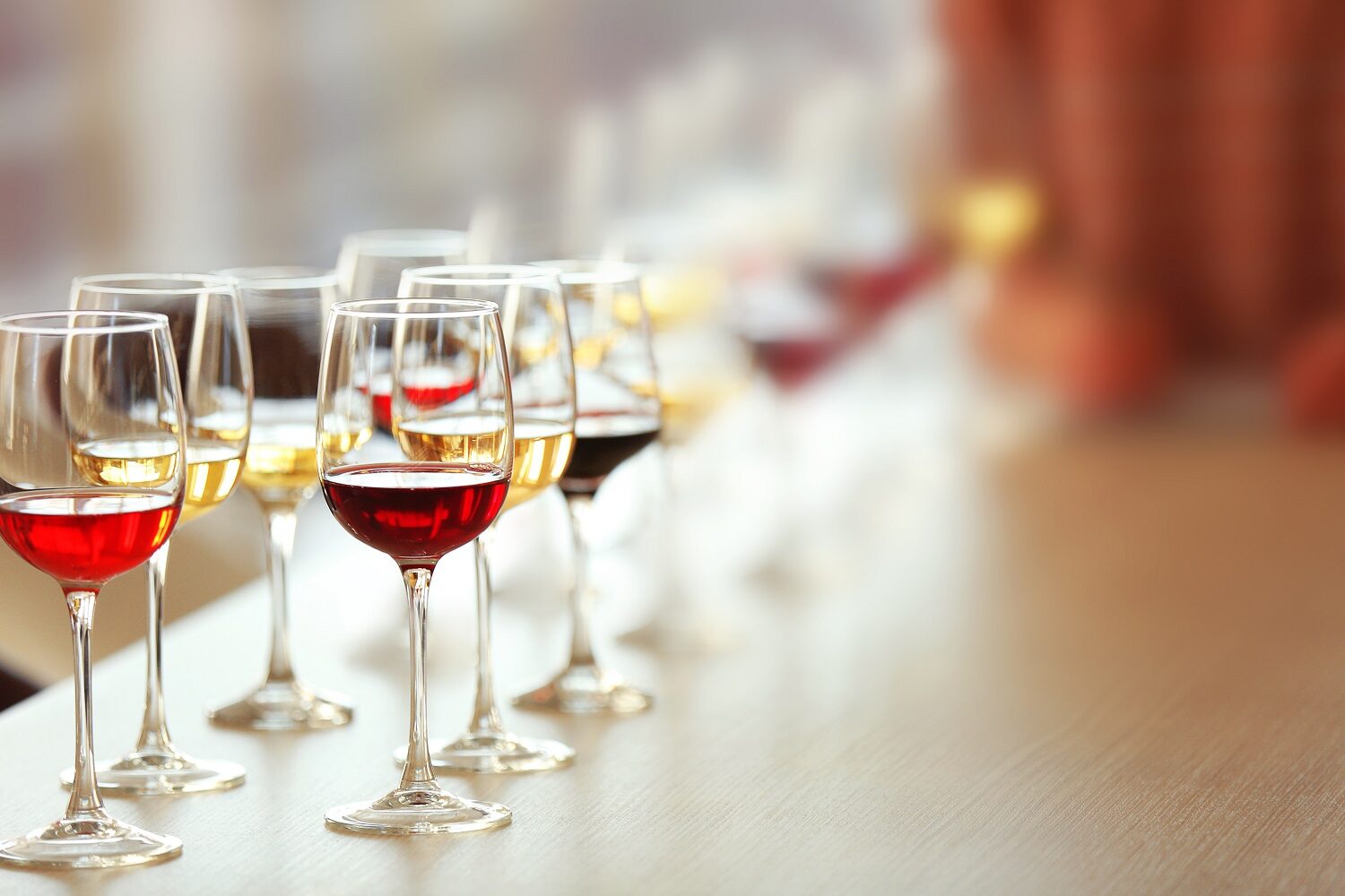 Mai multe pahare cu diferite tipuri de vin, alb si rosu, asezate in sir pe o masă