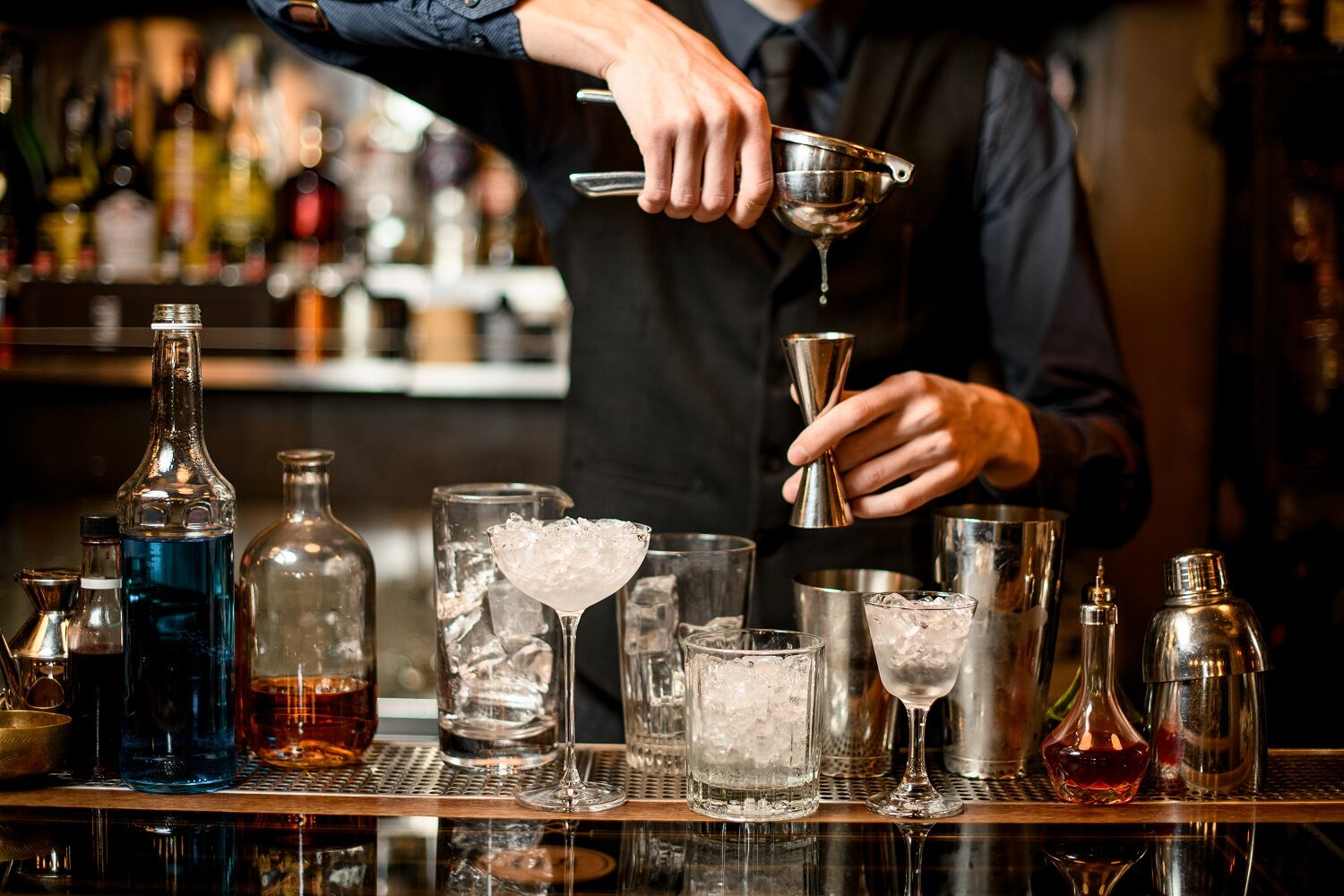 barman care stoarce o lămâie intr-un pahar, iar langa el, pe bar, sunt insirate mai multe pahare goale - imagine reprezentativă pentru cocktailuri faimoase