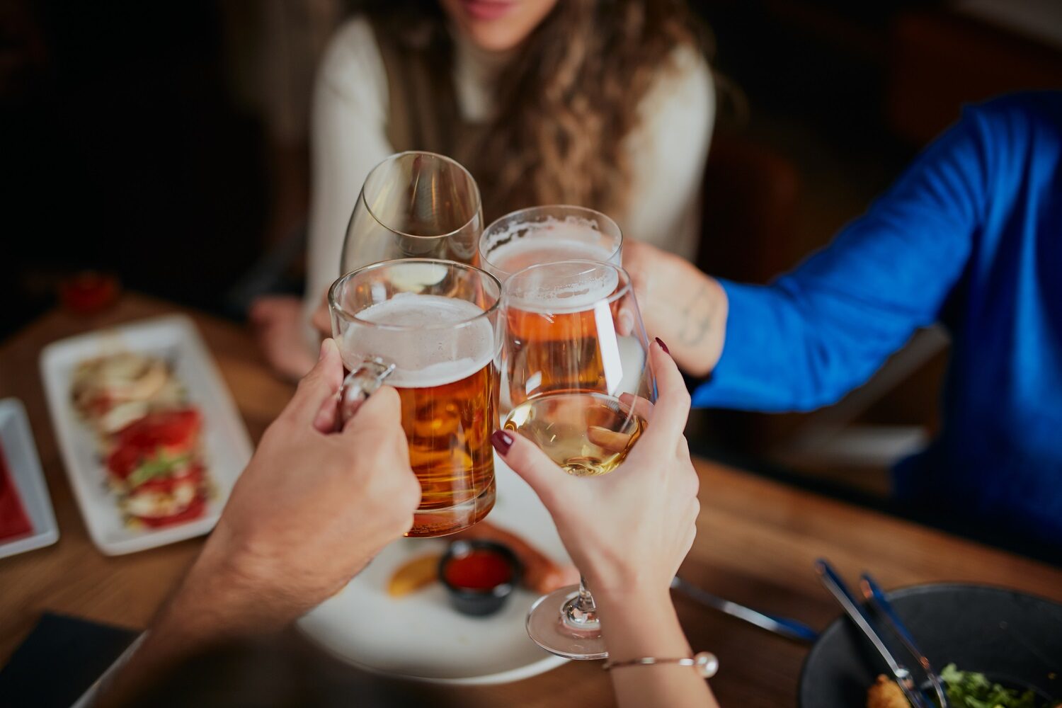 Grup de prieteni care sarbatoresc intr-un restaurant si ciocnesc un pahar de bere - imagine reprezentativă pentru cum asociezi berea cu mâncarea