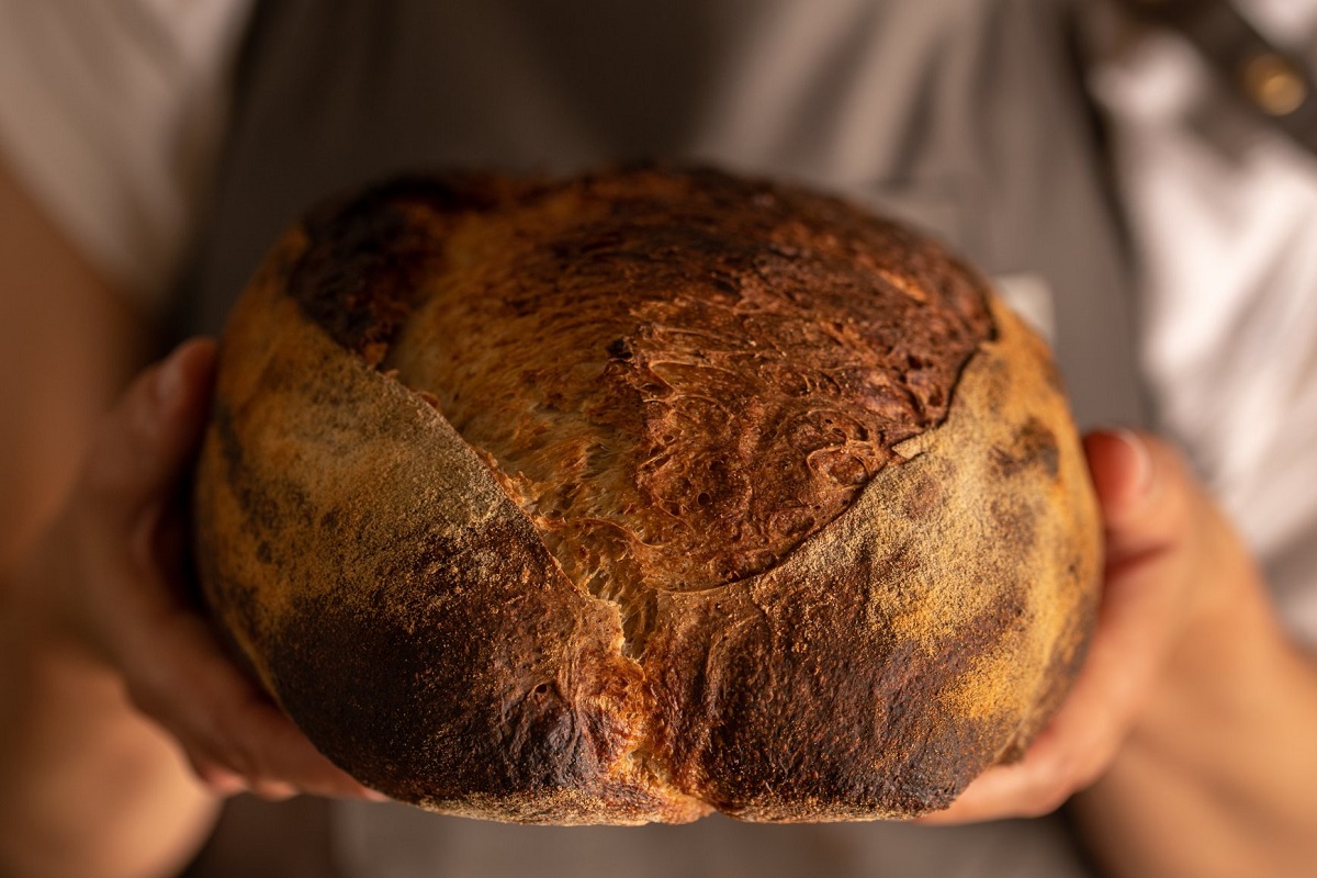 close up cu o persoana care tine in maini o paine mare si rumena, la Grain Trip București