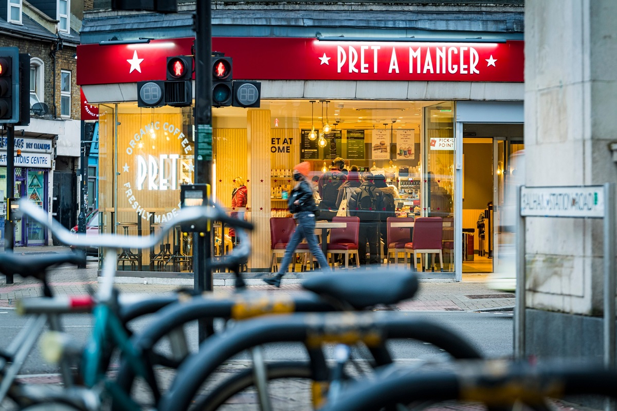 local pret a manger din Londra, fotografiat din strada, cu vitrine mari si firma rosie, cu biciclete in prim plan