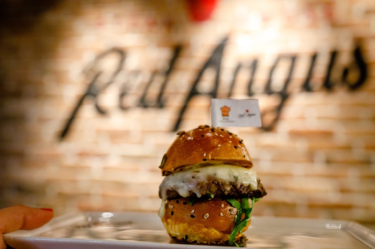 close up cu un burger cu carne de vită Angus, iar in fundal sigla restaurantului Red Angust Steakhouse
