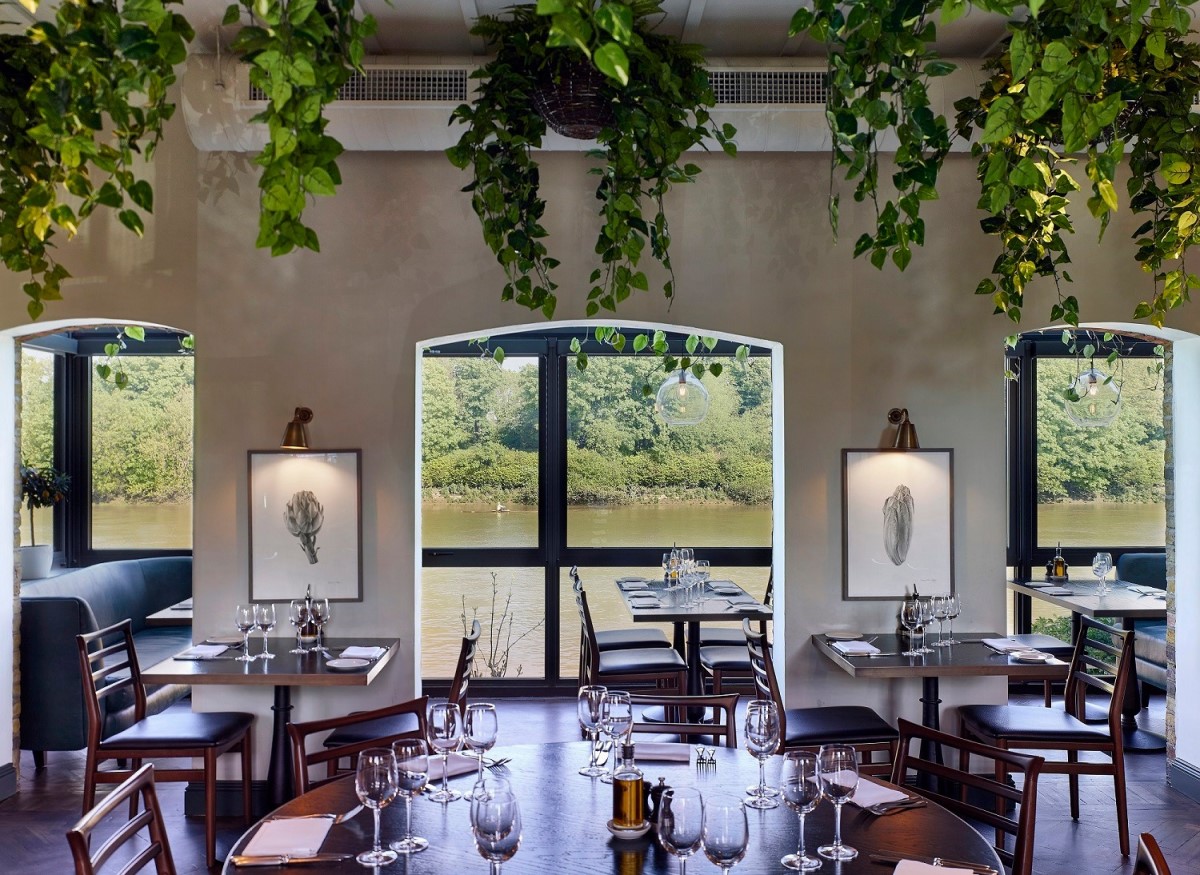 restaurant Rick Stein Barnes cu mese elegante, din lemn, tablouri pe pereti si in fundal ferestre arcuite prin care se vede apa unui râu