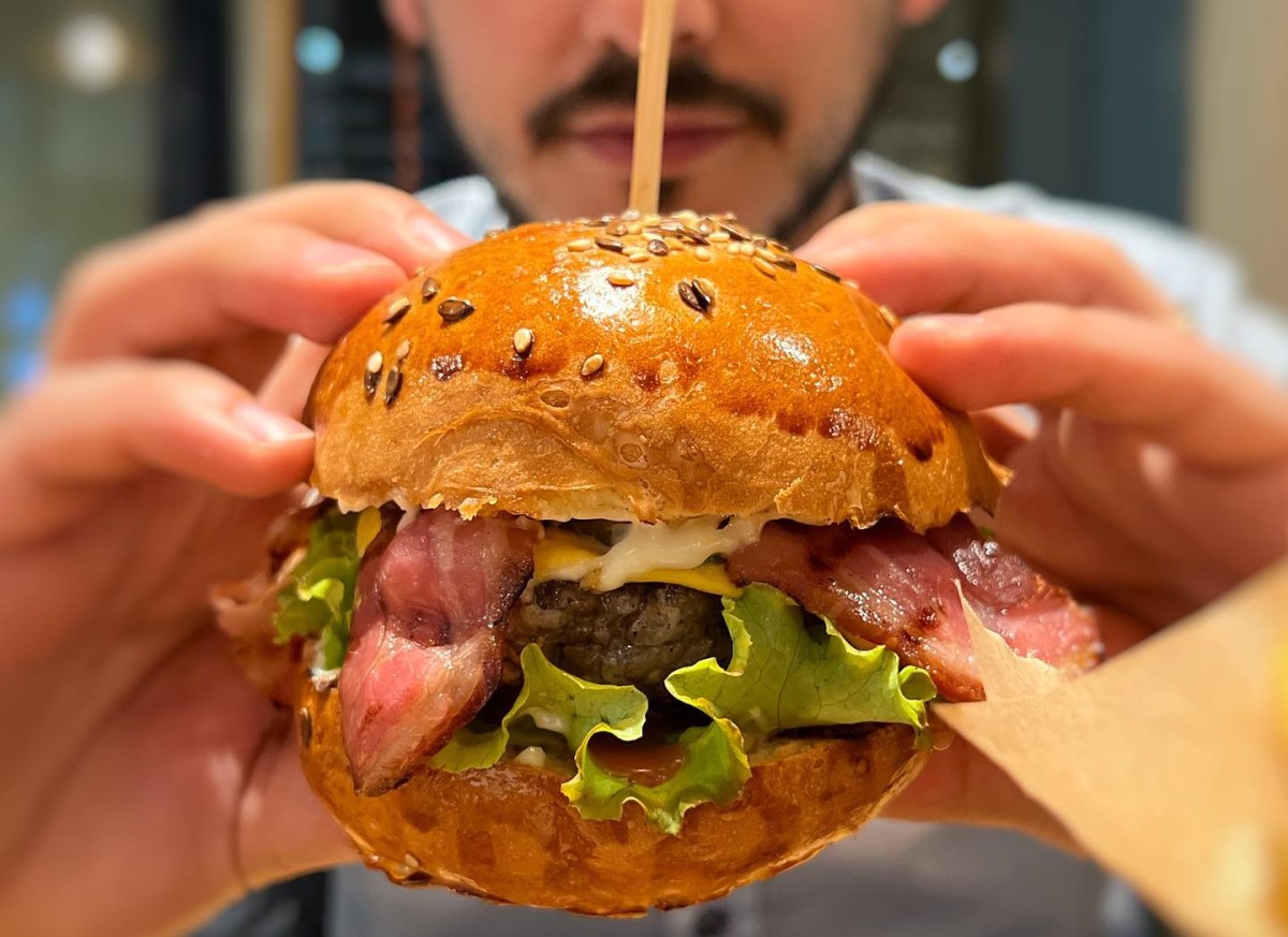 close up cu un barbat care tine in maini un burger cu salata, carne de vita, maioneza si bacon, la Stadio Restaurant