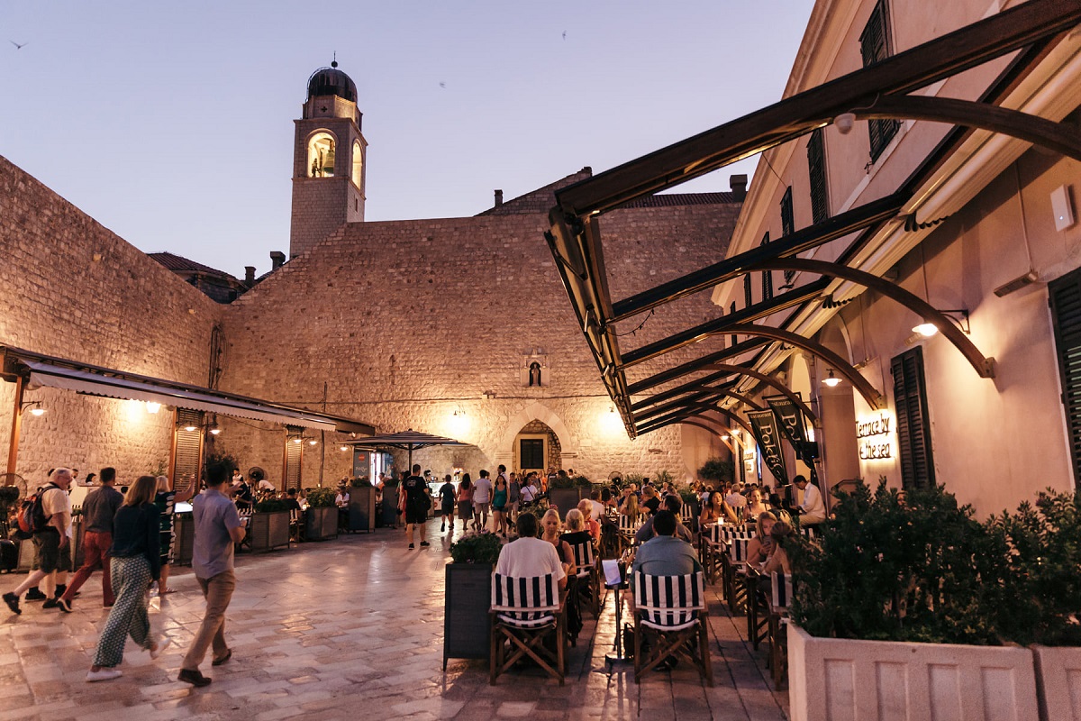 terasa restaurantului Poklisar din Dubrovnik, fotografiata seara, cu mese asezate pe strada in Cetatea veche, cu oameni asezati la masa, un loc perfect pentru experiențe culinare inedite și o destinație gastronomică din Europa