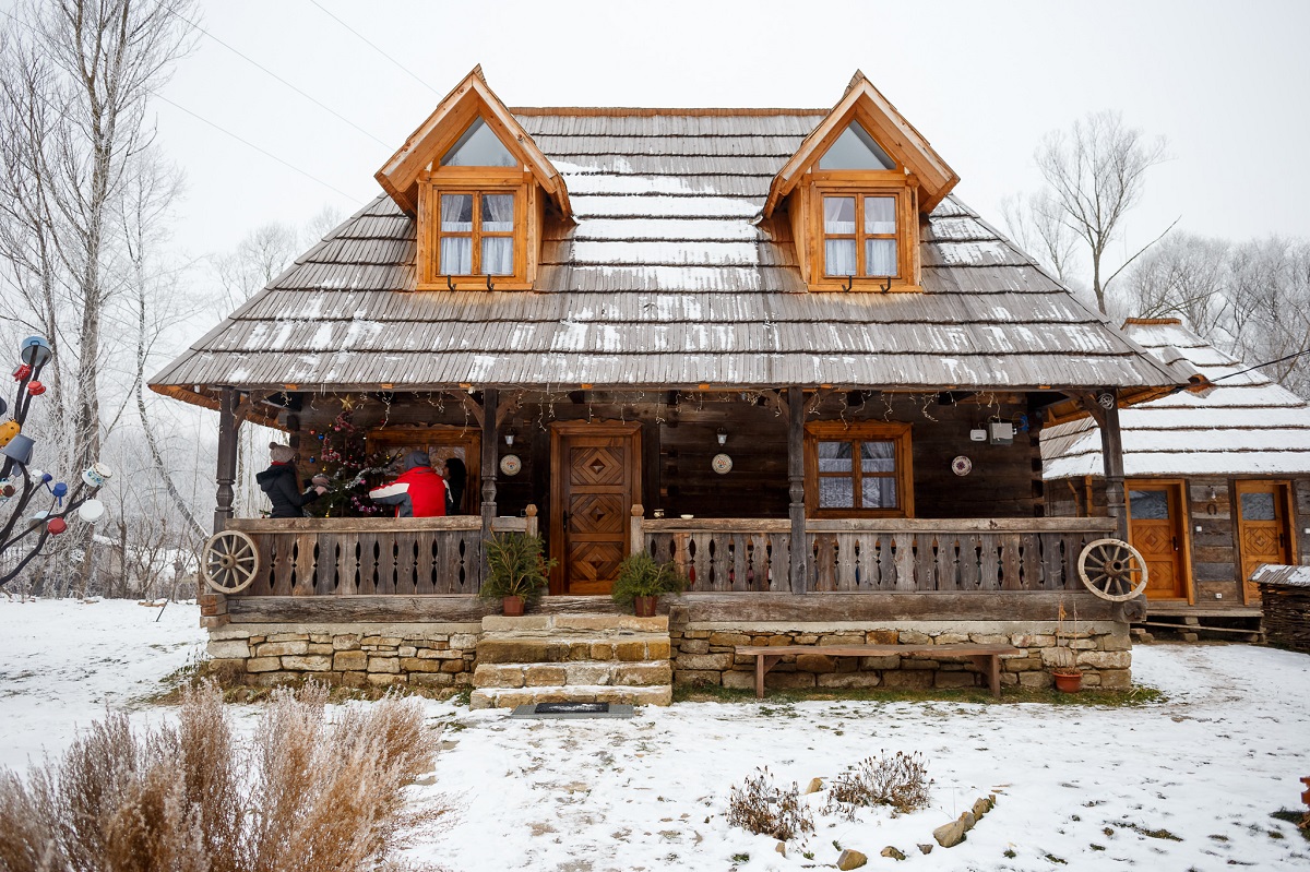 prim plan cu Căsuța din Scobai, mica, din lemn, cu pridvor, casa maramureseana fotografiata iarna, cu zapada in curte - destinație experiență de Crăciun