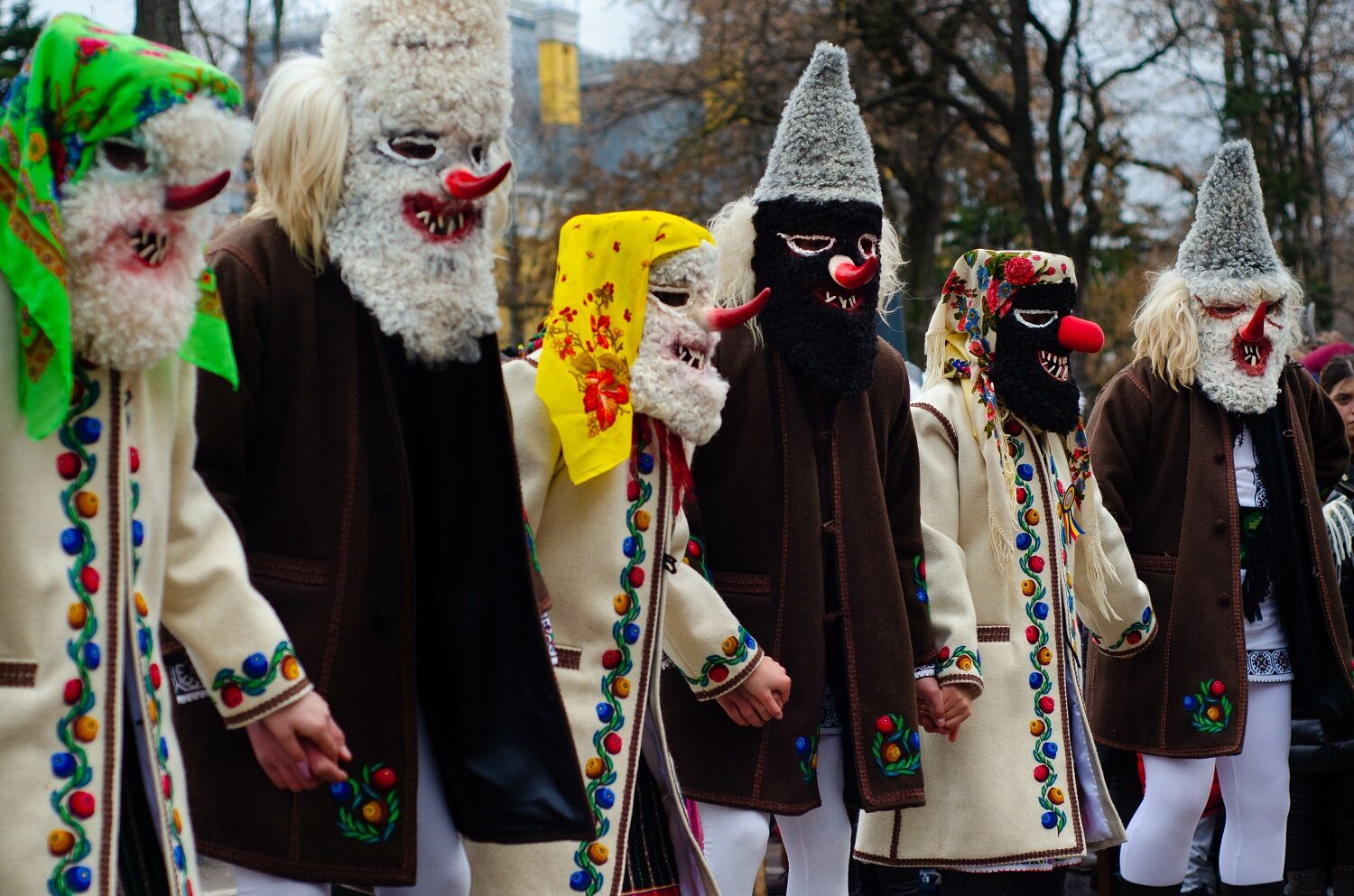 barbati si femei in costume traditionale romanesti, barbatii cu haine negre iar femeile cu haine albe, decorate cu flori tesute, purtand masti infricosatoare pe fata - traditii de sărbători pentru un Crăciun autentic românesc