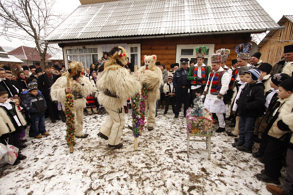 grum de colindatori intr-o curte a unei case batranesti, inconjurati de spectatori, imbracati in costume de blana de oaie si masti pe fata - traditii de Craciun In Transilvania, pentru un Crăciun autentic românesc